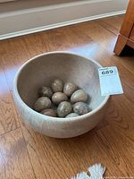 Stone bowl containing ten stone eggs on hardwood floor, shot from above and side angles