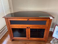 Front view of the wooden TV stand showing black glass top, glass doors with wooden frames and black panels, and knobs.