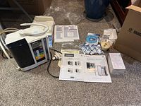 Machine, manuals, DVD, enhancer bottles and small accessories arranged on floor.