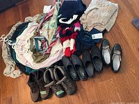 Wide view of assorted women's clothing and shoes laid out on floor including sweaters, shirts, boots, and flats.