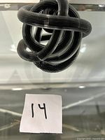Glass art sculpture resembling a knotted shape with black and white stripes, shown on a reflective surface with a note marked '14'.