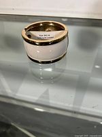 Wide white enamel and gold-tone bangle bracelet showing front bracelet design and style label.