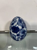 Front view of the white ceramic egg decorated with intricate blue floral and paisley designs.
