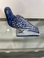 Side view of blue and white ceramic bird figurine showing detailed feather painting and rectangular base.