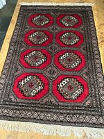Full view of the rectangular Bokhara rug laid flat on a wooden floor, showing its pattern and fringe ends.