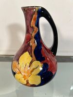 Front view of the ceramic English jug showing colorful floral decoration including a yellow flower pattern and a black handle.