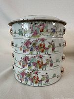 Front view of the 4-tier porcelain stacking box showing hand-painted famille rose style scenes with multiple figures and landscape details.