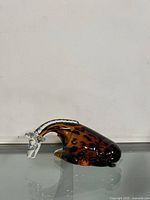 Side view of Italian glass giraffe figurine showing amber glass body with black leopard spots and clear glass neck and head, placed on a reflective surface.