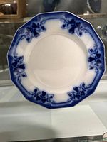 Top view of octagonal ceramic plate showing blue floral and grapevine design along scalloped edges on white background.