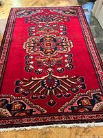 Full view of handmade Khamse wool rug with central medallion and decorative borders on red field.