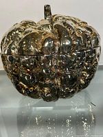 Front view of the metal pumpkin bowl showing the textured pumpkin shape with lid on top and reflective surface.