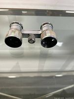 Opera glasses with mother of pearl inlay and metal construction from a top angle showing focus knob.