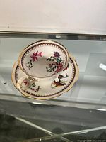 Tea cup set inside the matching saucer showing floral and bird decoration with gold accents.