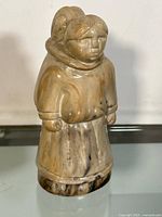 Front side of the figurine showing a woman wearing traditional clothing carrying a child on her back.