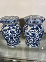 Pair of small blue and white Asian garden stools with traditional floral designs on a glossy porcelain surface, standing side by side.
