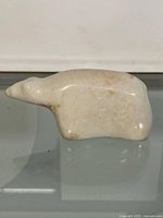 View of the bear figurine from the side showing its elongated snout, smooth surface, and natural stone coloration.