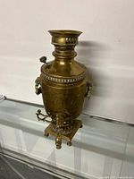 Front view of vintage brass samovar, showing spout handle and missing one leg