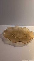 Side angled view of translucent amber glass scalloped dish showing embossed center and etched leaf details