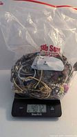 Clear sealed plastic bag containing assorted jewelry pieces weighing over 4 pounds shown on digital scale.