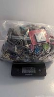 Plastic bag filled with assorted jewelry and miscellaneous items placed on a digital scale showing 7 pounds weight.
