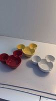 Three Mickey Mouse-shaped ceramic dip bowls in red, yellow, and white, showing front view of bowls with three compartments each.