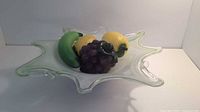Green wavy glass bowl containing glass fruit including a banana, lemons, and grapes