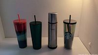 Four collectible Starbucks mugs and tumblers arranged side by side showing designs and colors.