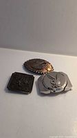Lot of three belt buckles: copper eagle, black vintage car, silver floral.