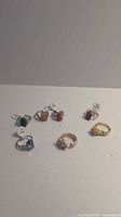 Photo showing all seven costume rings laid out in two rows on a white background. Rings feature a variety of stone colors and metal finishes.