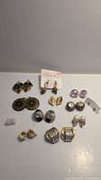Full view of assorted vintage costume earring sets laid out on a white surface including clip-on and stud styles in various materials and colors.