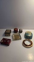 Seven assorted small decorative items on white surface including trinket boxes and magnifying glass