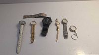 All seven watches displayed on flat light surface showing variety of bands and face designs