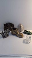 Photo showing the metal crown, bronze boot, ceramic face, green ceramic shoe, bronze coin purse, and clear glass cube candle holder grouped on a flat surface.
