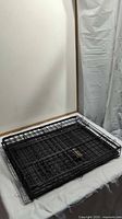 Folded black metal wire pet carrier cage on white surface against neutral background
