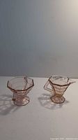 Both creamer and sugar bowl shown side by side on white surface, highlighting the pink depression glass and geometric pattern.