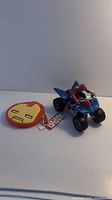 Spider-Man figurine riding blue ATV toy next to Iron Man change purse with Marvel tag