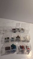 Overview of 12 small clear plastic boxes with mixed beads and stones inside, some with metal components