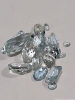 Close-up image of eleven loose aquamarine gemstones on a light surface, clear to pale blue in color, faceted in various shapes including oval, marquise, pear, and round cuts.