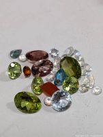 Loose assorted genuine gemstones in various colors and cuts on a white background, totaling about 10 carats weight.
