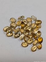 Loose oval cut genuine citrine gemstones in yellow to golden shades spread on a white surface.