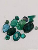Multiple loose emerald gemstones in varied shapes and colors on white background.