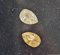 Close-up of two pear shaped fancy color diamonds on black background, showing color and internal characteristics.