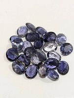 Cluster of approximately 27 loose faceted oval iolite gemstones in varying shades of blue and violet, showing the natural color and clarity range.