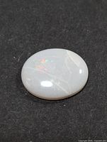 Top view of oval genuine opal on black background showing iridescent play-of-color and surface details.