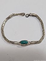 Sterling silver bracelet with turquoise stone centerpiece, hooked clasp, on white background.