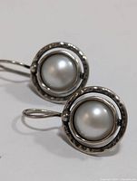 Close-up of one earring showing round white pearl and hammered silver bezel