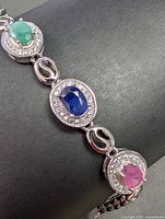 Close-up image of the sterling silver bracelet showing emerald, sapphire, and ruby stones with clear stone halos and linked silver design.