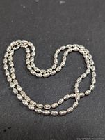 Full length shot of the silver necklace showing oval bead chain coiled on black background.