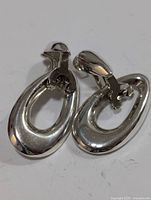 Front angled view of two silver oval clip-on earrings showing polished surface and oval hollow shape.
