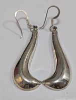 Pair of silver drop earrings with teardrop shapes laid flat on a white surface.